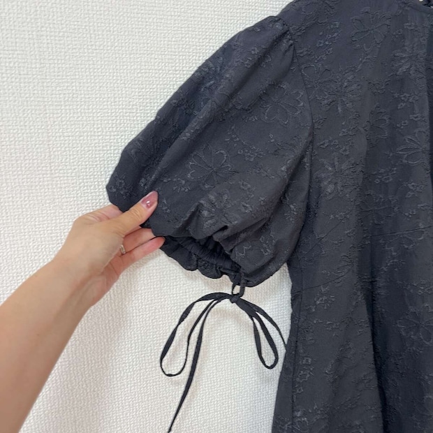 黒いバルーンスリーブチュニックの袖とリボンを指でつまんでいる