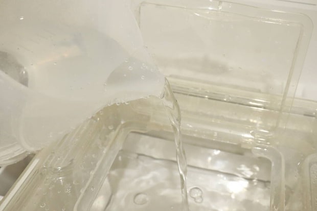 計量カップからウォーターサーバーのタンクへ水を注いでいる様子