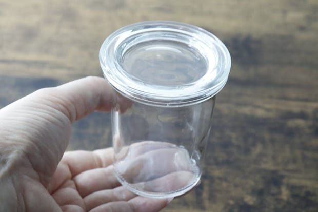 手のひらに乗せられた透明なガラス容器。蓋は外されており、容器の口が見える。