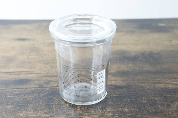 木目のテーブルに置かれた透明なガラス容器。側面には商品情報シールが貼られている。
