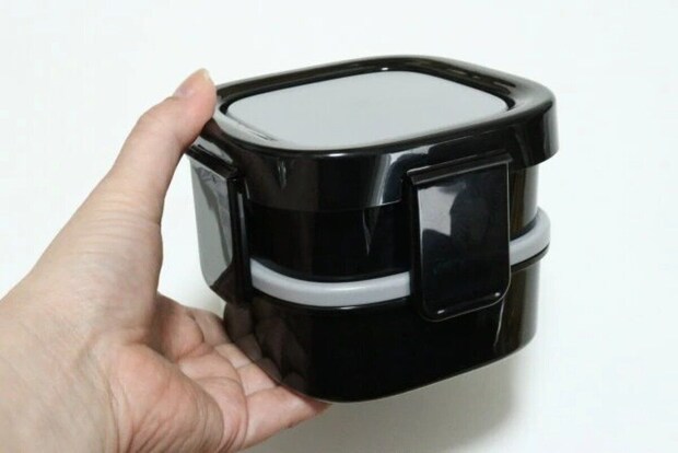 黒い2段式の弁当箱を片手で持っている様子