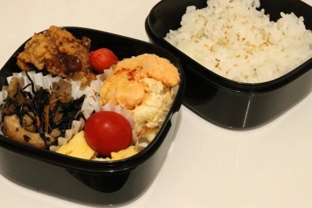 黒い2段式の弁当箱に、ご飯とおかず（唐揚げ、卵、ミニトマトなど）が詰められている