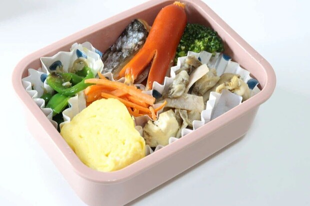 ピンク色の弁当箱の下段に、卵焼き、ウインナー、野菜などのおかずが詰められている