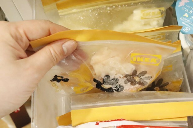 冷凍庫から小分けにされた食品の袋を女性の手が取り出している