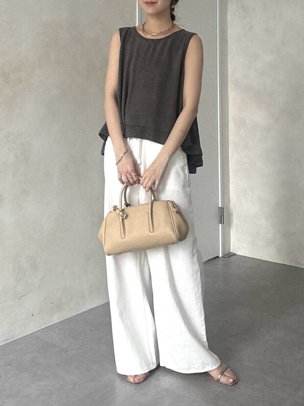 チャコールグレーノースリーブと白ワイドパンツの女性がベージュバッグを持つ