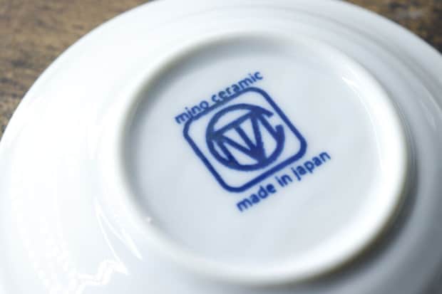 白い豆皿の裏側に「mino ceramic made in japan」のロゴが青字で印字されている