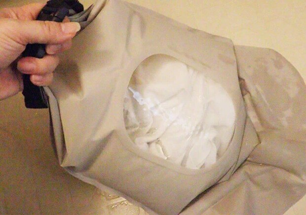 ウォッシュバッグに白い衣類と水を入れて揉み洗いする手元