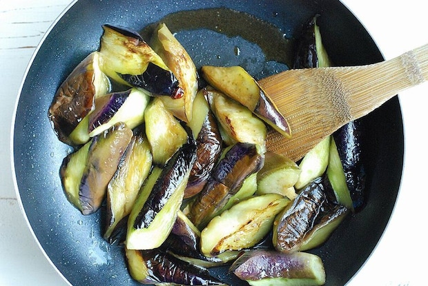 フライパンでなすを木べらで炒め、皮に焼き色がついている フライパンでなすを木べらで炒め、皮に焼き色がついている