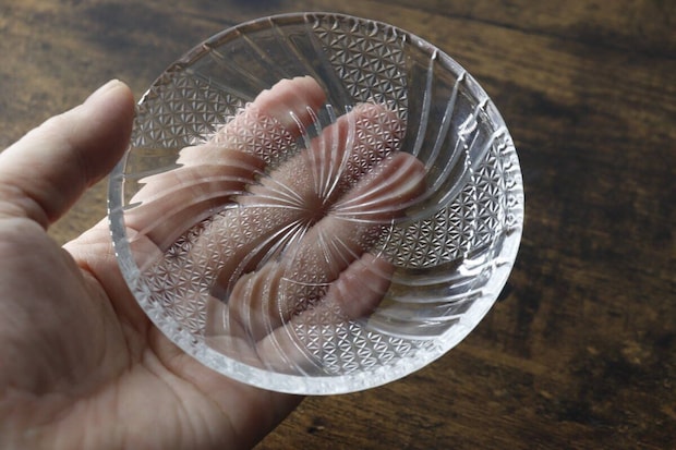 手のひらにガラス小皿を乗せ、光に透かして模様の美しさを確認している写真 手のひらにガラス小皿を乗せ、光に透かして模様の美しさを確認している写真