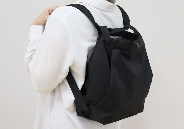 白シャツの女性が黒いバッグをリュックとして背負う 白シャツの女性が黒いバッグをリュックとして背負う