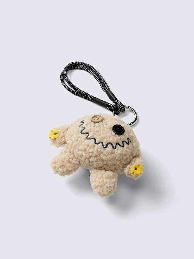 ベージュのふわふわしたモンスター型チャーム。ボタンの目と口が特徴