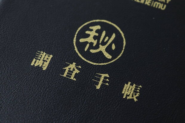 ムーのレザー調ノートの表紙に施されたゴールドの箔押し「秘」「調査手帳」の文字のクローズアップ