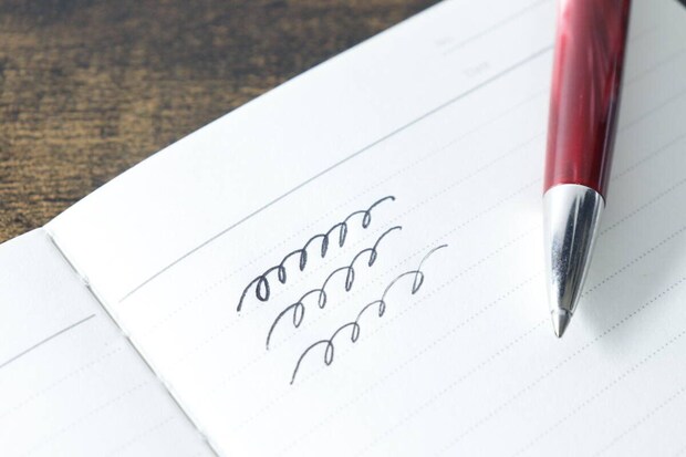 ムーのレザー調ノートに赤いボールペンで文字を試し書きしている手元のクローズアップ