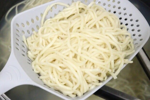 グレーのザルスプーンで鍋から茹でた麺をすくい上げている