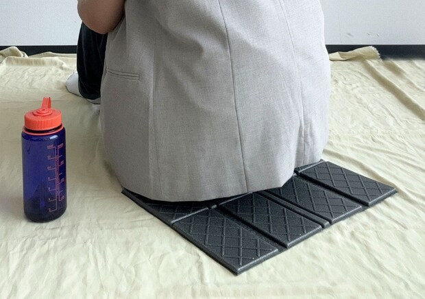 レジャーマットに座っている人の下半身と水筒