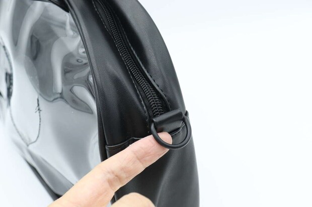 黒いクリアバッグ側面にあるショルダーストラップ用Dカンを指で示している 黒いクリアバッグ側面にあるショルダーストラップ用Dカンを指で示している
