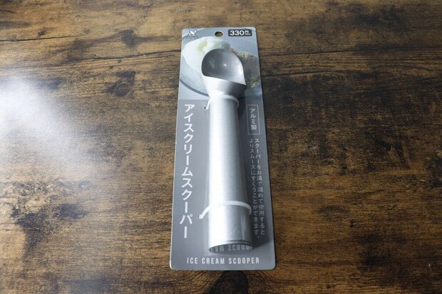 パッケージに入ったアルミ製アイスクリームスクーパーが木目のテーブルに置かれている
