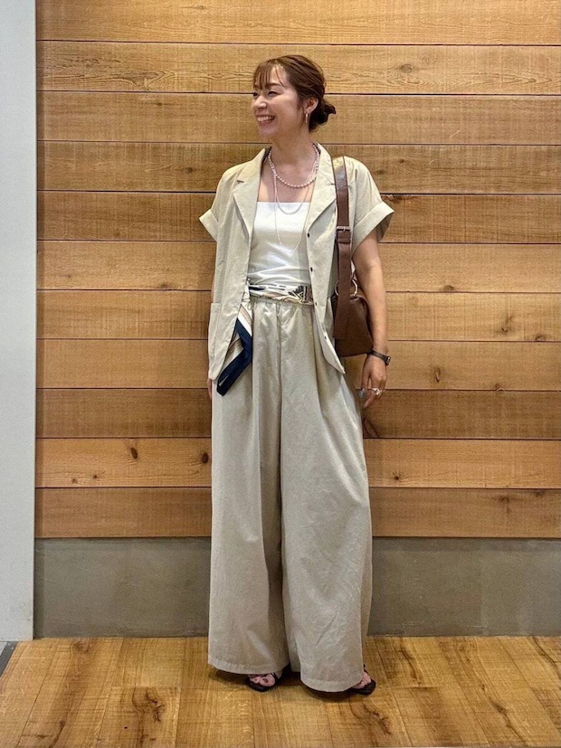 ベージュのシャツジャケットとワイドパンツを着た女性が笑顔で横を向く ベージュのシャツジャケットとワイドパンツを着た女性が笑顔で横を向く