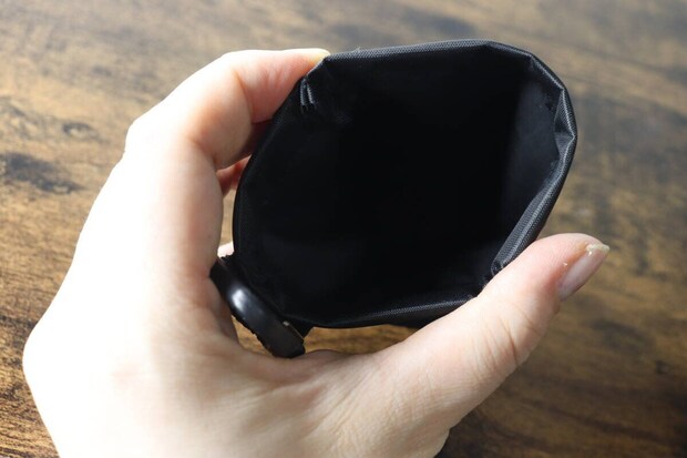女性の手が黒い携帯ごみポーチのバネ口を開き、内側が見えている 女性の手が黒い携帯ごみポーチのバネ口を開き、内側が見えている