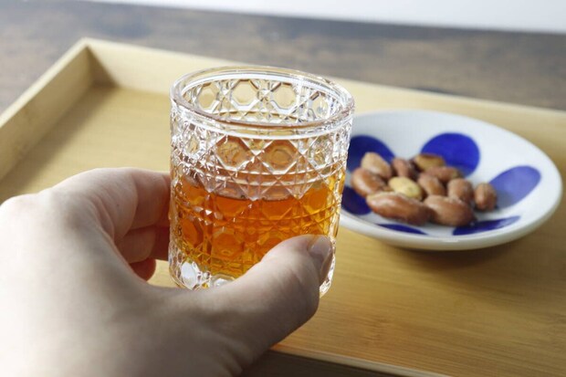 ミニグラスに入った琥珀色の飲み物と、おつまみのピーナッツを持つ手 ミニグラスに入った琥珀色の飲み物と、おつまみのピーナッツを持つ手
