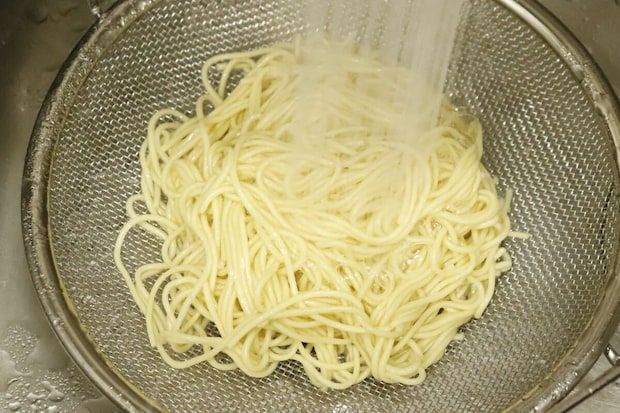 シンクで浅型ザルを使いラーメンのような麺を湯切りしている様子 シンクで浅型ザルを使いラーメンのような麺を湯切りしている様子