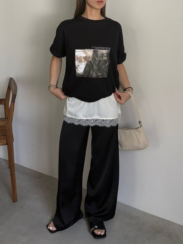 黒のフォトTシャツとサテンワイドパンツ、白レースキャミを重ねた女性