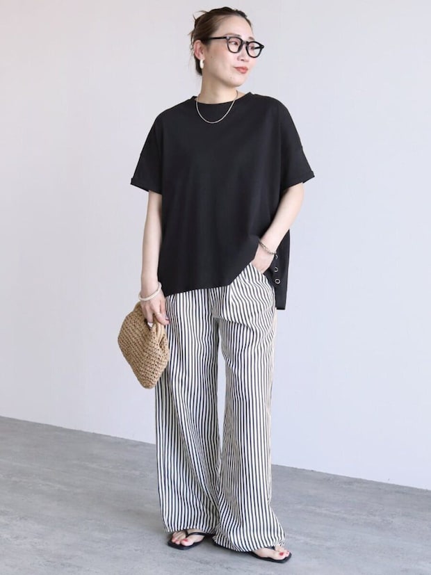 黒Tシャツにストライプ柄ワイドパンツを合わせ、かごバッグを持つ女性