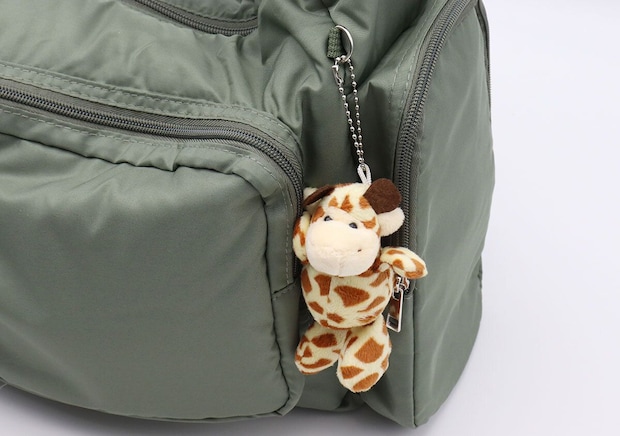 緑色のショルダーバッグのDカンに、キリンのぬいぐるみチャームが付けられている