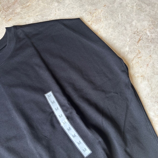 黒いTシャツの肩部分がアップで写っており、タグが複数枚重なっている