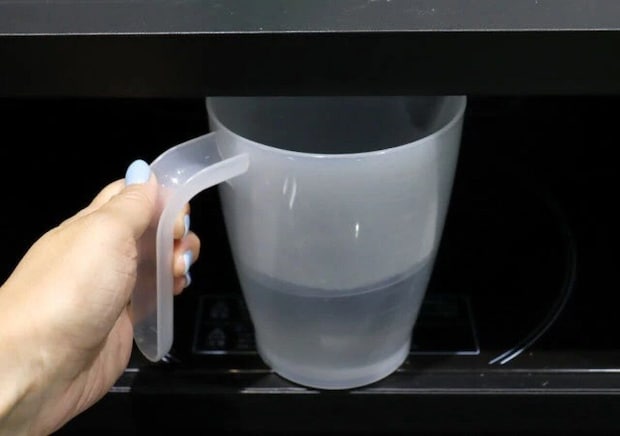 女性が水を入れた万能メジャーカップを電子レンジに入れようとしている
