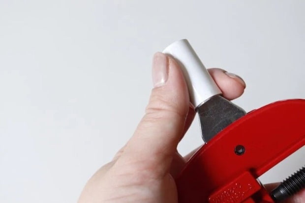 赤いパイプカッターの面取り刃で白いパイプの切り口をなめらかにしている様子