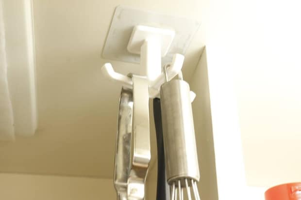 キッチン戸棚の下に設置した回転フックに泡立て器とトングを吊り下げた様子