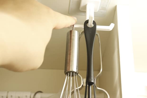 フックに吊るした泡立て器とトングを指で回し、回転機能を示している様子