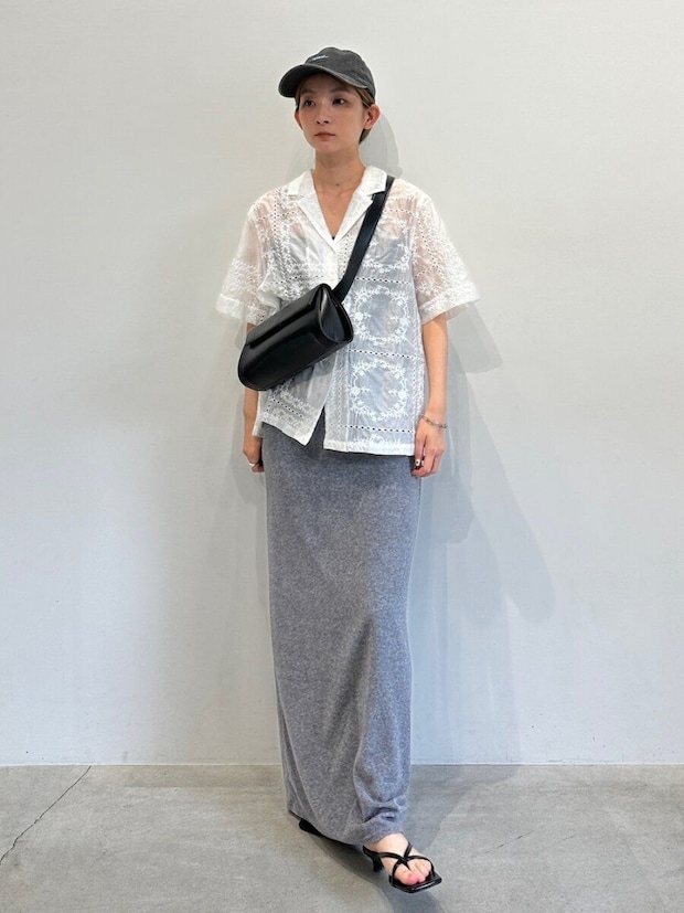 白いレースシャツとグレーのIラインスカートを着た女性が黒いキャップとバッグを身につけている