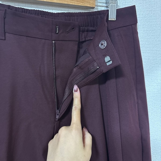女性がワイン色のタックワイドパンツのファスナーとホックを指す