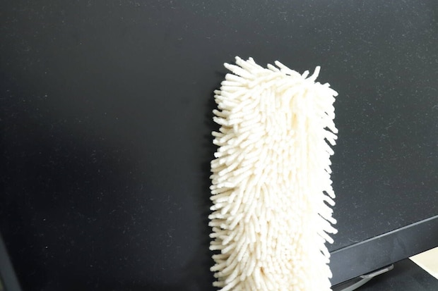 黒いモニター画面のホコリを白いハンディモップで拭いている様子