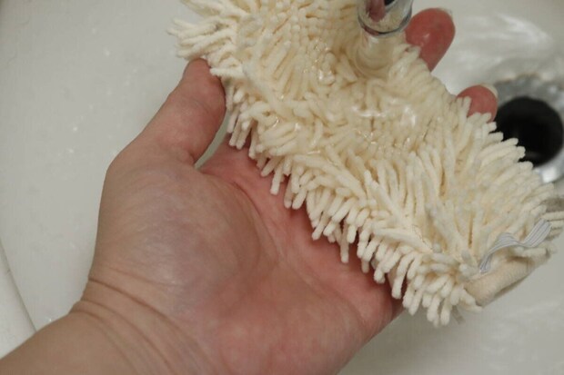 流水で白いハンディモップの汚れを洗い流している手元