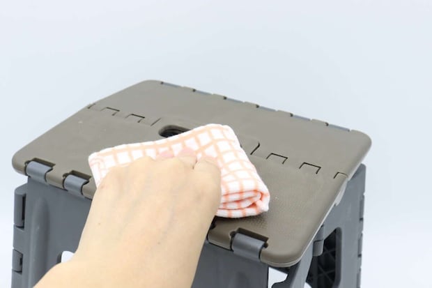 折りたたみイスの座面を布巾で拭いている手元