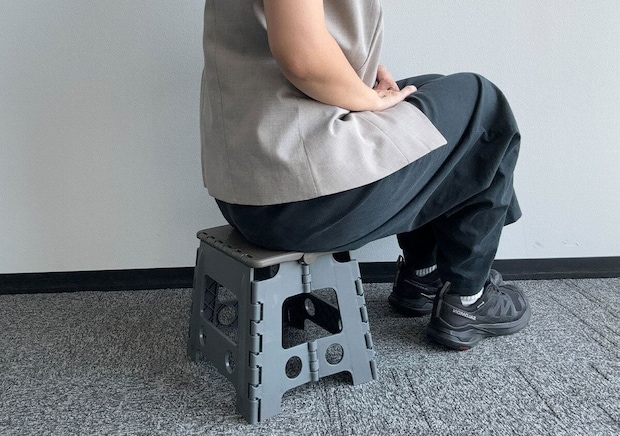 展開した折りたたみイスに座る女性の横からの全身