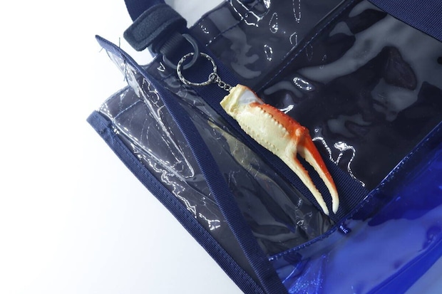 青いビニール素材のバッグのポケットからカニ爪キーホルダーが覗いている様子