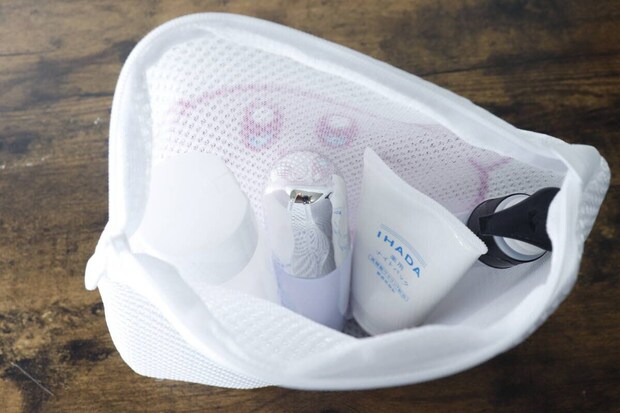 洗濯ネットの中に化粧水ボトルや美顔器など旅行用アメニティグッズが入っている 洗濯ネットの中に化粧水ボトルや美顔器など旅行用アメニティグッズが入っている