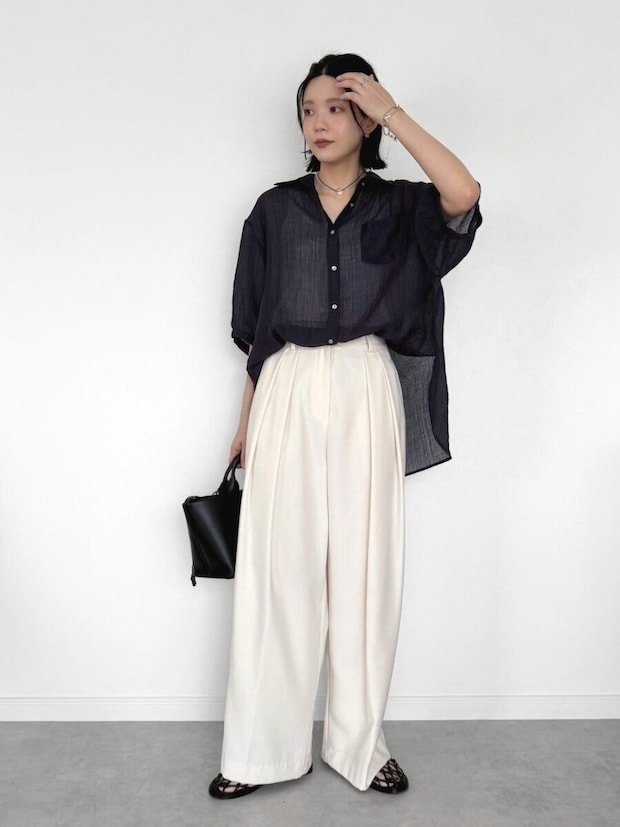 黒シアーシャツと白ワイドパンツ姿の女性が髪を触る