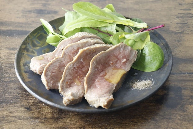 皿に盛り付けられた牛のたたきとベビーリーフにオリーブオイルがかかっている