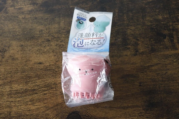 パッケージに入ったピンク色の洗顔ブラシが木目のテーブルに置かれている パッケージに入ったピンク色の洗顔ブラシが木目のテーブルに置かれている
