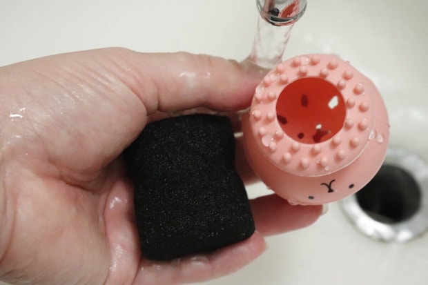 洗顔ブラシから黒いスポンジを取り出し、水で洗っている様子