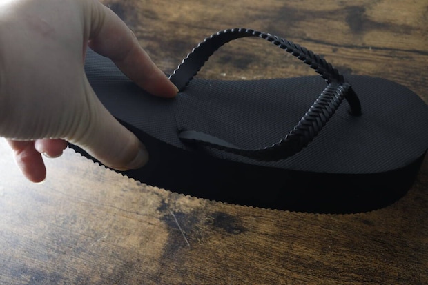 指で黒い厚底ビーチサンダルのソール部分を押して弾力を確認している 指で黒い厚底ビーチサンダルのソール部分を押して弾力を確認している