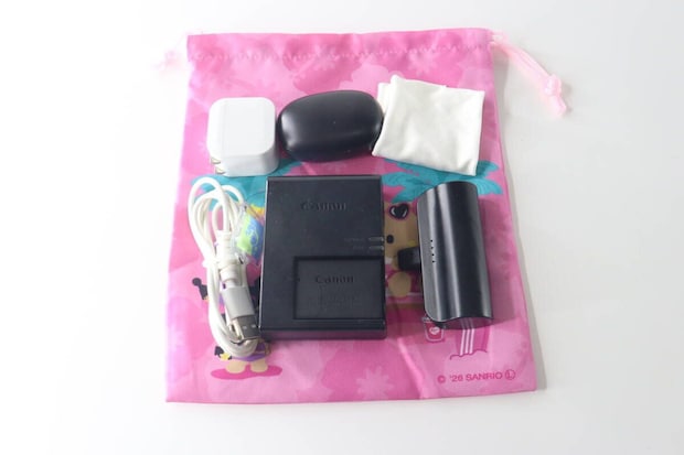 ピンク色の巾着袋の上に、充電器、ケーブル、ワイヤレスイヤホンなどのガジェット類が並べられている ピンク色の巾着袋の上に、充電器、ケーブル、ワイヤレスイヤホンなどのガジェット類が並べられている