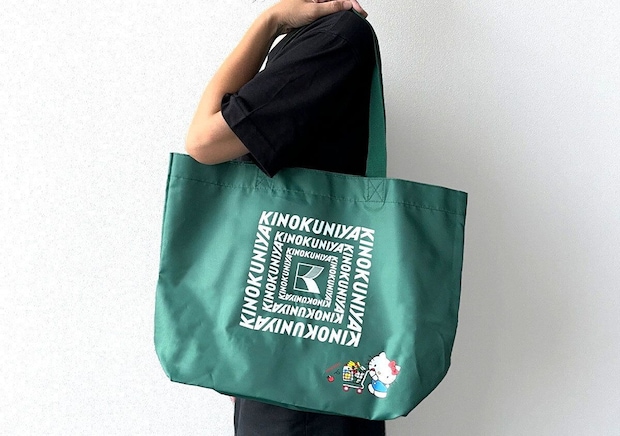 黒い服を着た人が緑色の紀ノ国屋×ハローキティお買い物バッグを肩にかけている