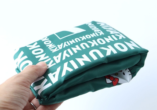 手が緑色の紀ノ国屋×ハローキティお買い物バッグをコンパクトに折りたたんでいる