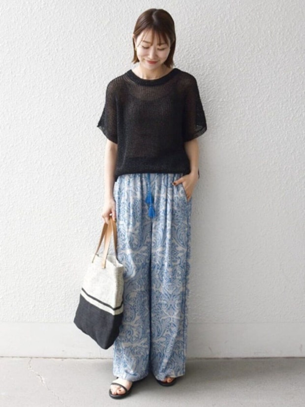 透け感黒ニットと青柄ワイドパンツ、トートバッグを持った女性
